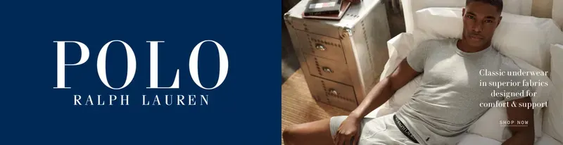 A wide retail web banner: a navy panel carrying the brand wordmark beside a photograph of a model in a white t-shirt and grey shorts sitting on a bed, with a shop-now link.