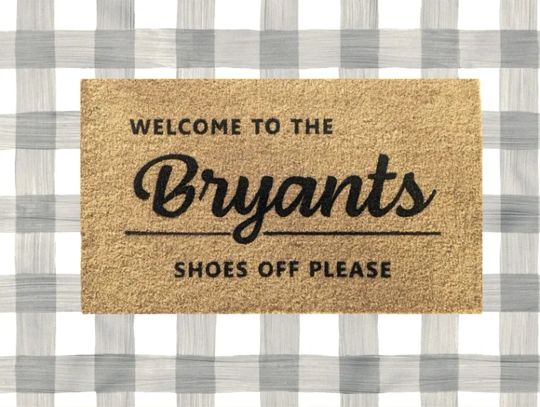 A coir doormat on a grey and white check floor, lettered "Welcome to the Bryants" in a script with "Shoes off please" beneath it.