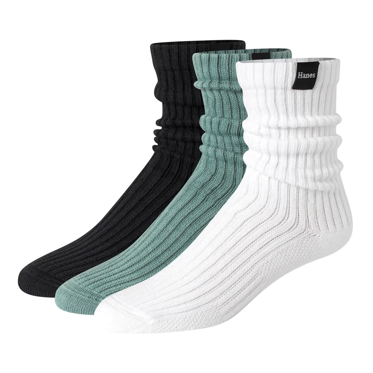 Three ribbed slouch crew socks standing upright side by side on white, in black, sage green and white, each with a small woven label at the cuff.