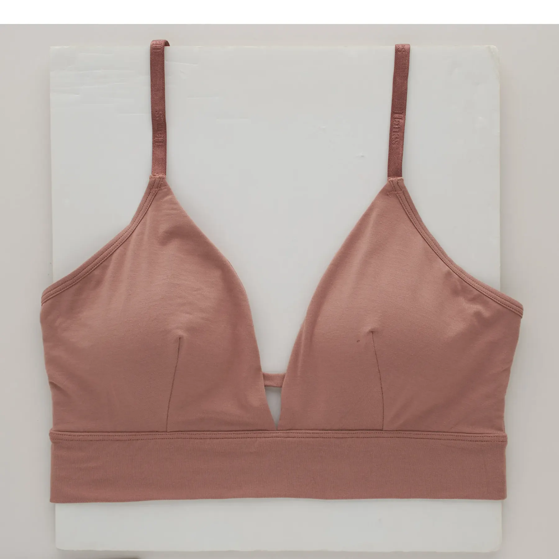 The same bralette as shot, lying on a grey surface with a soft shadow along one edge and the straps falling unevenly.