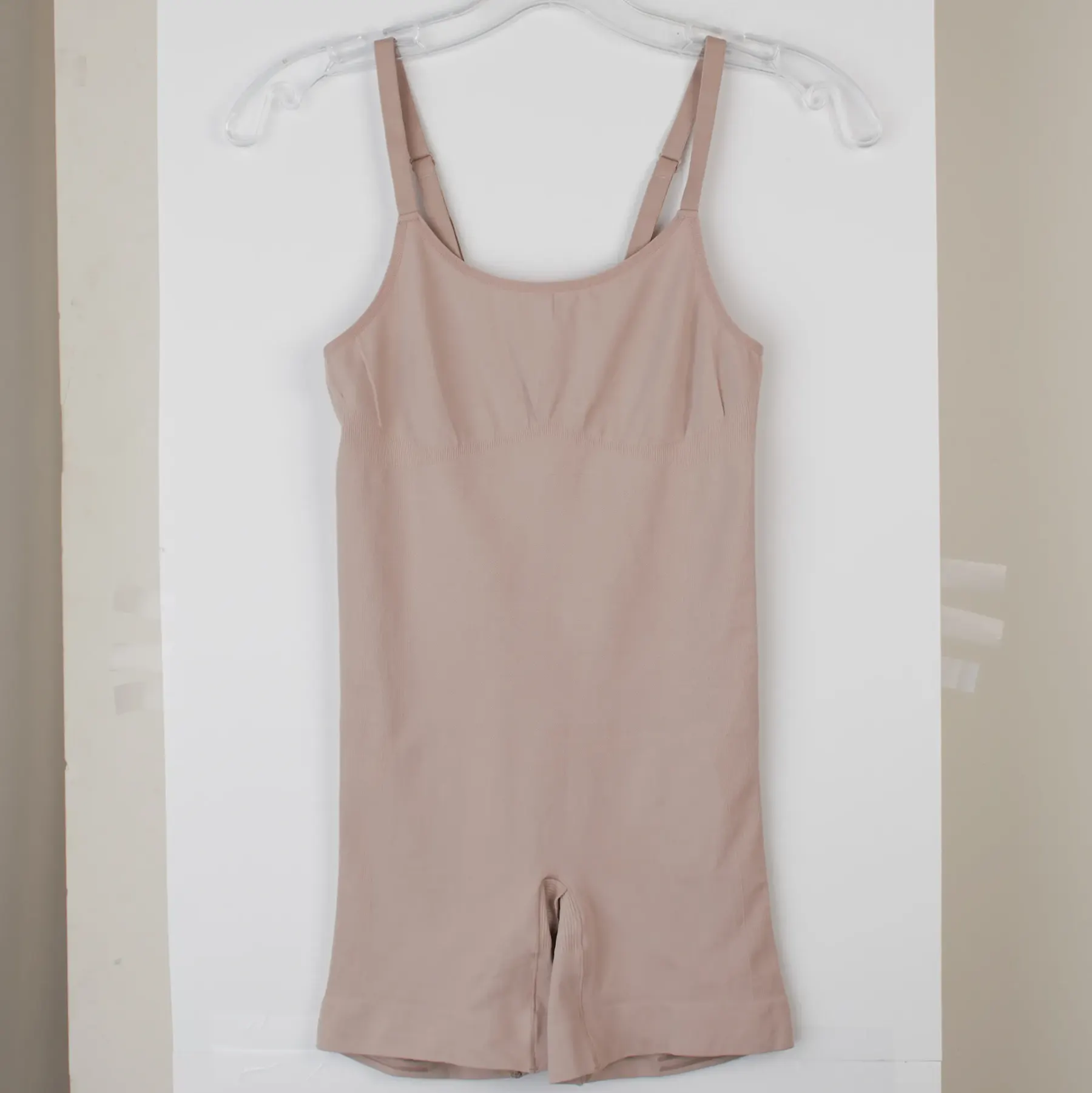 The same garment as shot on a white hanger against a stockroom wall, hanging slightly askew with the wall's shadow behind it.