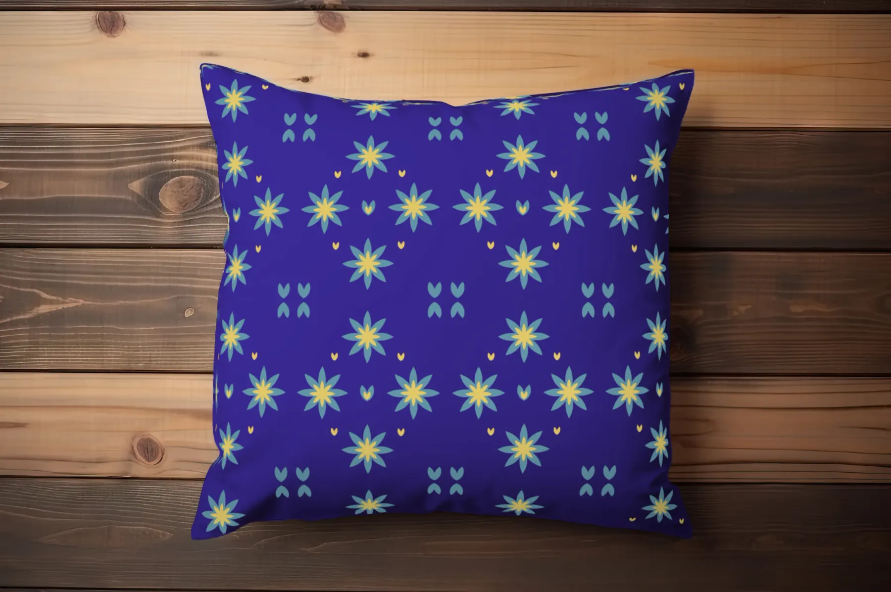 The pattern printed on a deep blue cushion lying on stained pine boards, the teal and yellow star flowers running edge to edge.
