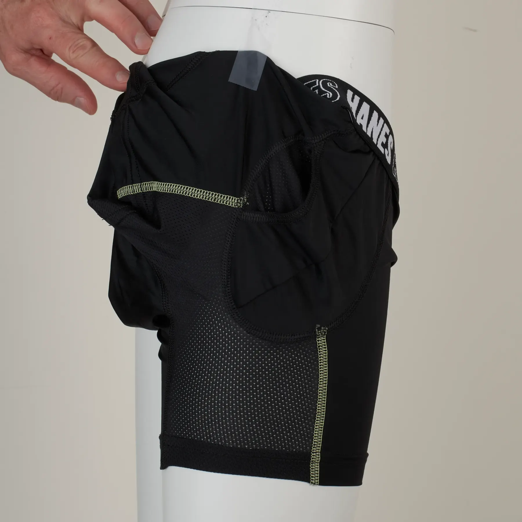 Another frame from the shoot: a hand reaches in at the top to hold the waistband against the form, and the garment is lit unevenly.